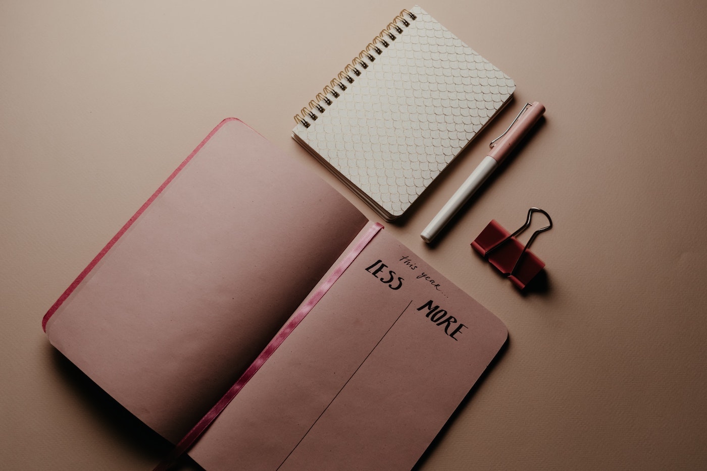 Bilan 2022 Strat&CI carnet rose ouvert sur une table avec un tableau à deux colonnes correspondant aux objectifs de l'année à venir (colonne "ce que je veux plus" et "ce que je veux moins"), un stylo un autre carnet de notes et un attache de documents