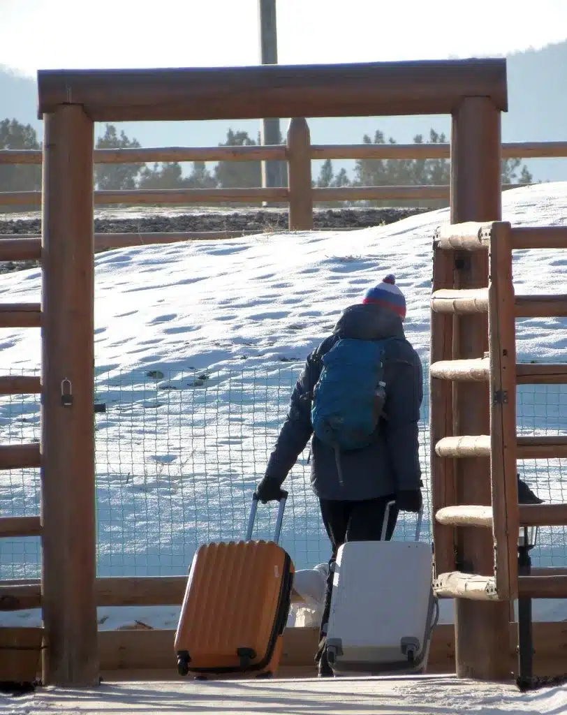 Touriste habillé chaudement qui tire 2 valises sous un porche extérieur dans un paysage enneigé